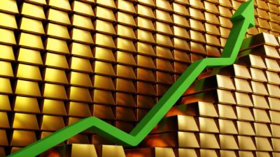 Rising gold share price represented by a green arrow on piles of gold block.