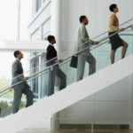 Five businessmen in suits walking up stairs in neat succession.