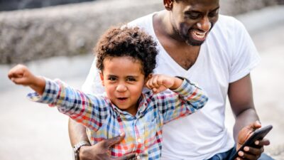A happy boy with his dad dabs like a hero while his father checks his phone.